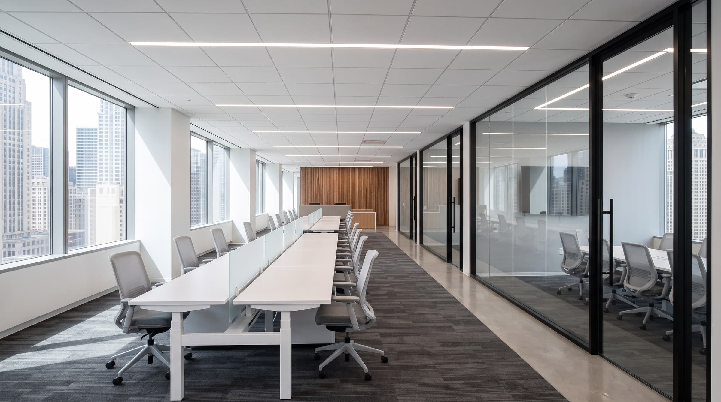 The finished office floor on handover day: sit-stand desks along the windows and a row of glass-front meeting rooms