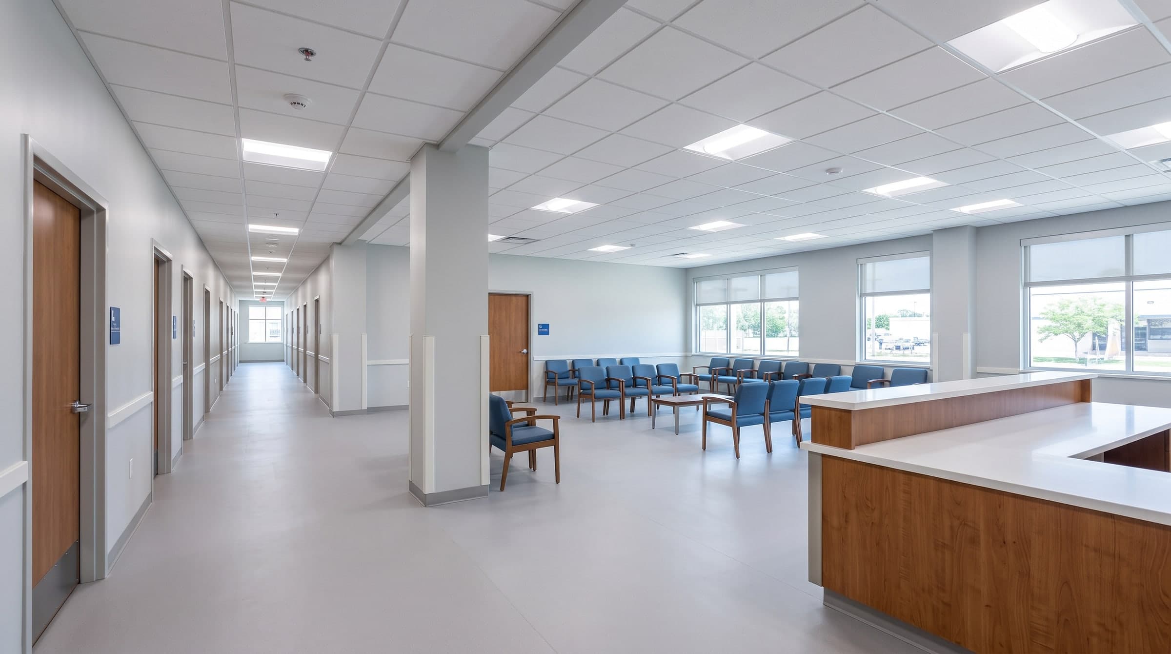 The finished floor before opening day: a corridor of exam room doors on the left, a waiting area with blue chairs and a check-in counter by the windows