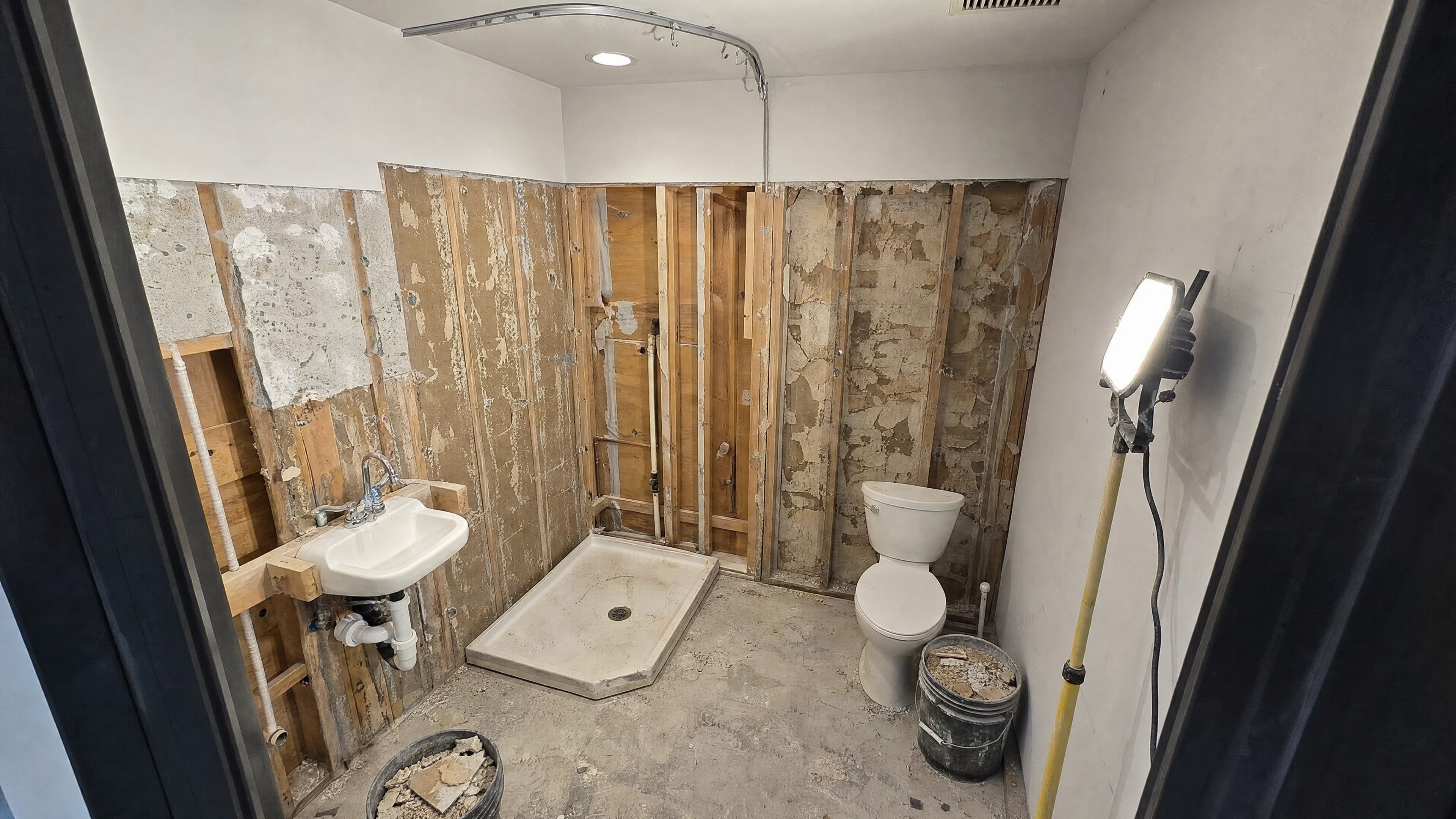 A shower room stripped to the studs with old tile removed and plumbing exposed