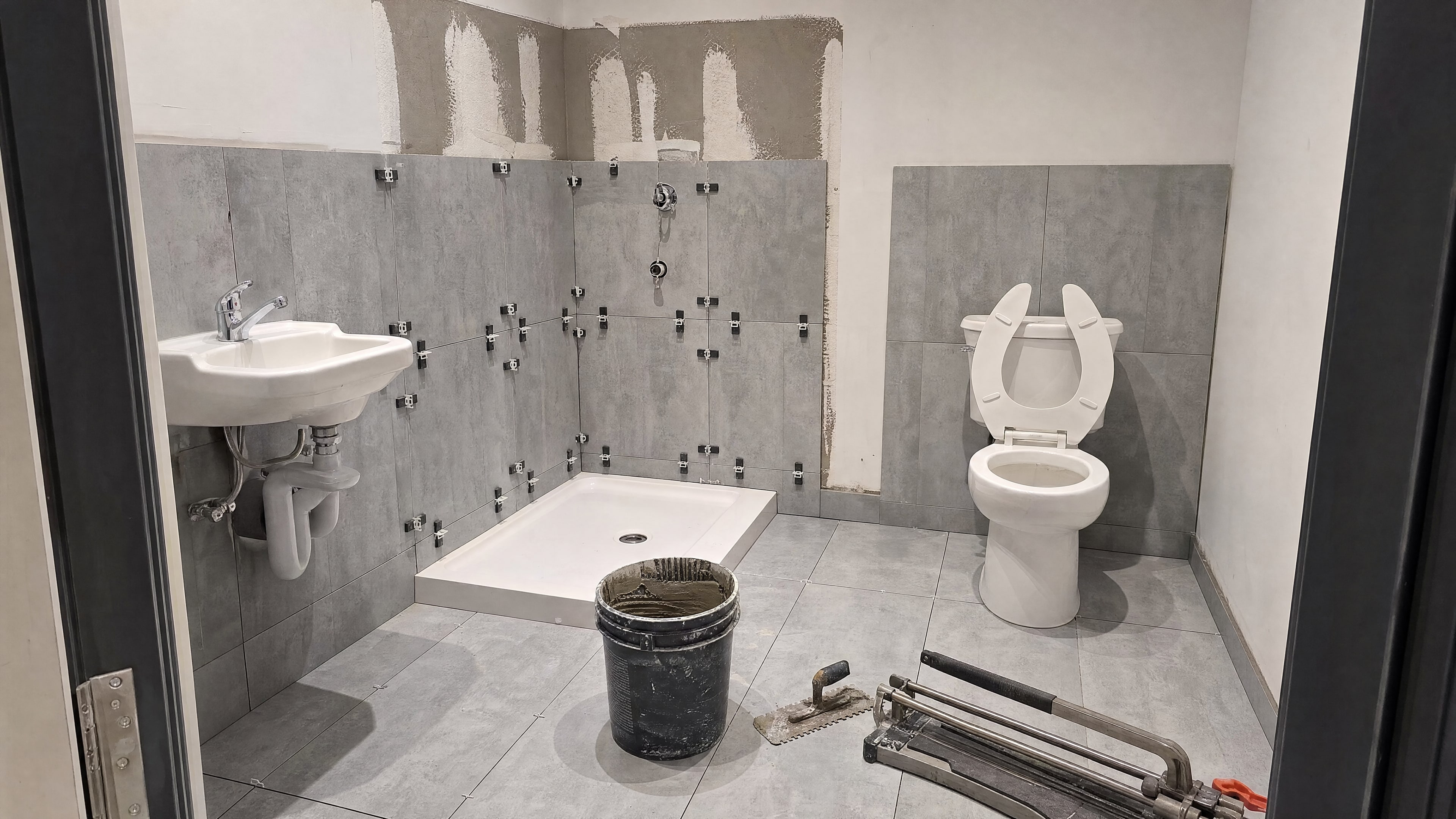 Large-format grey tile being installed on shower walls with leveling clips