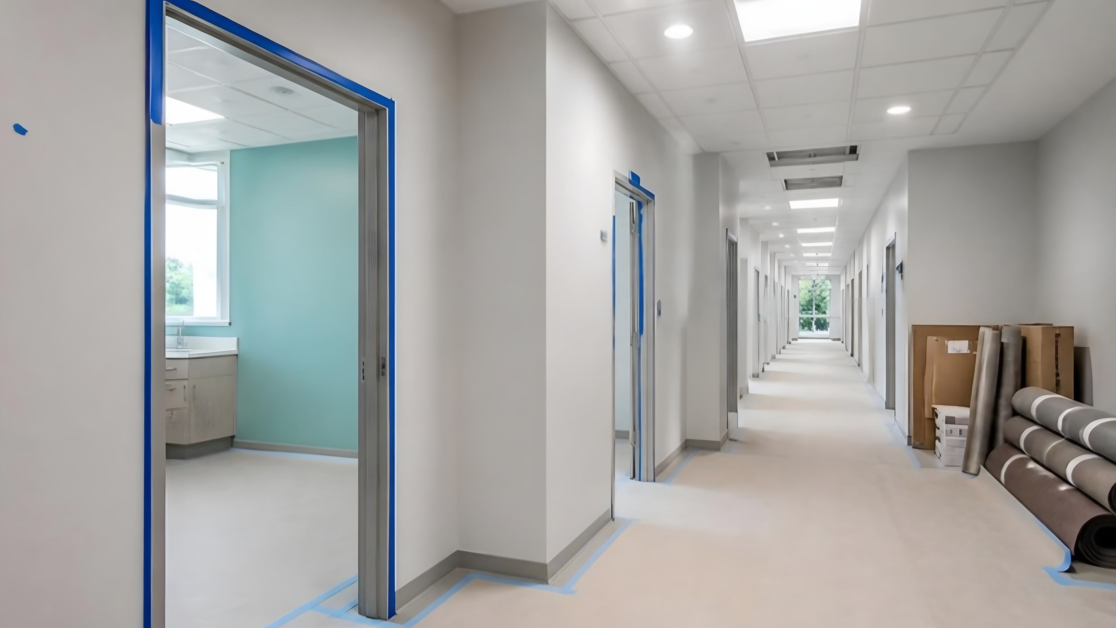 A clinic corridor with primed walls, an aqua accent wall, a finished ceiling and flooring rolls waiting to be laid