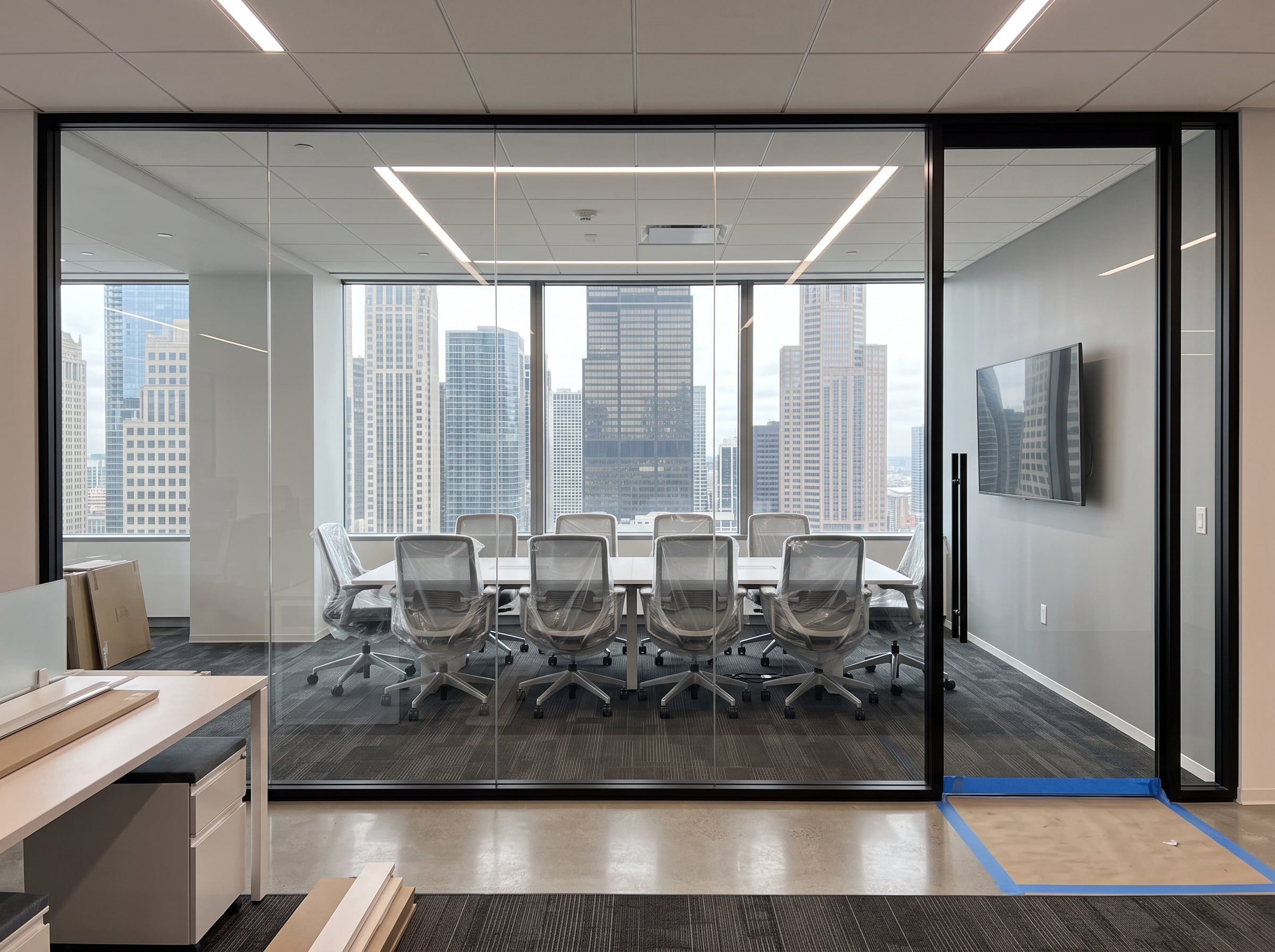 The same meeting room at handover: glass front, conference table with chairs still wrapped, display on the wall