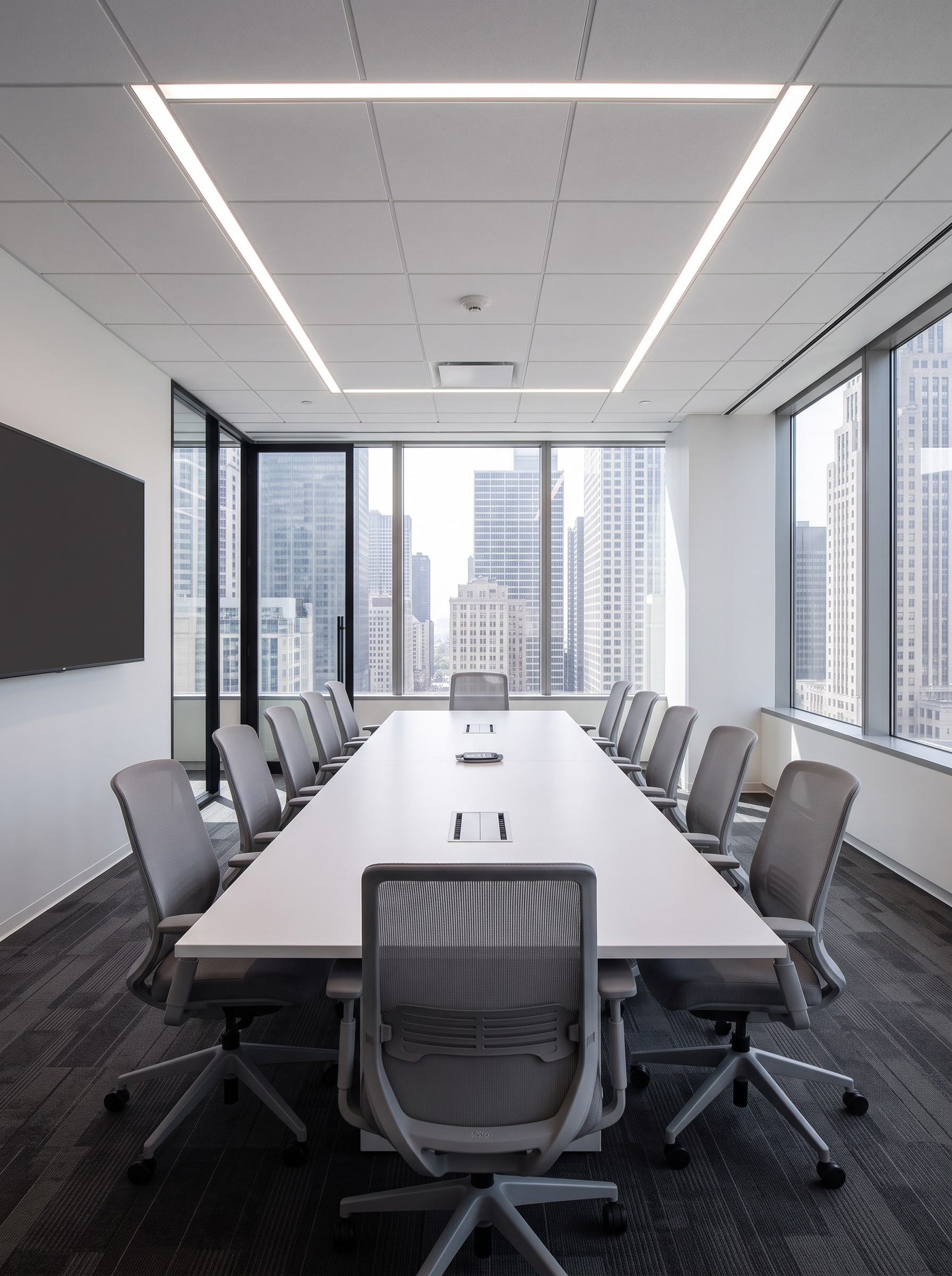 Inside a glass-front meeting room: conference table, mesh chairs, a wall display and the city beyond