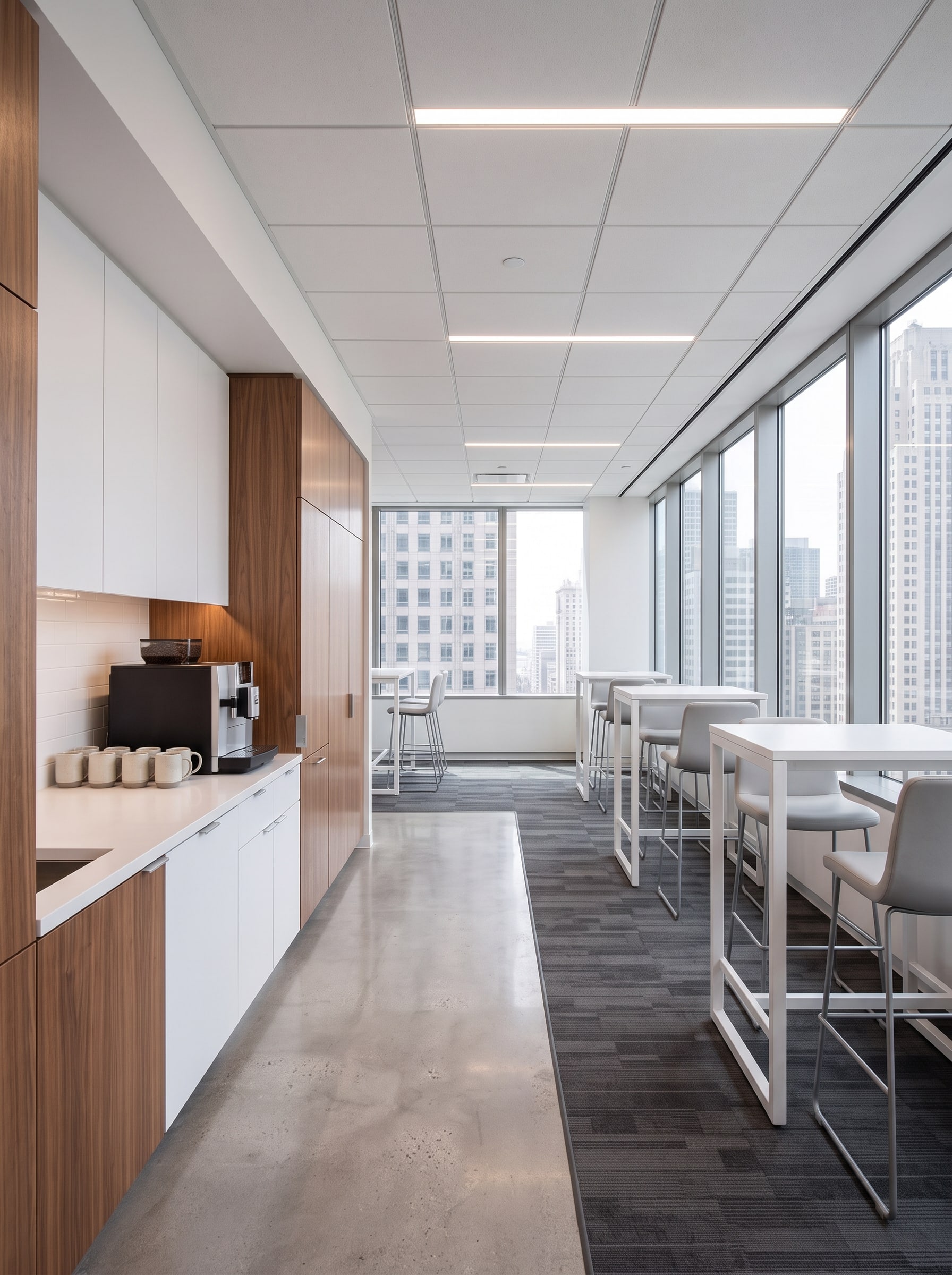 The break area: white kitchenette with wood-veneer cabinets and high-top tables by the windows