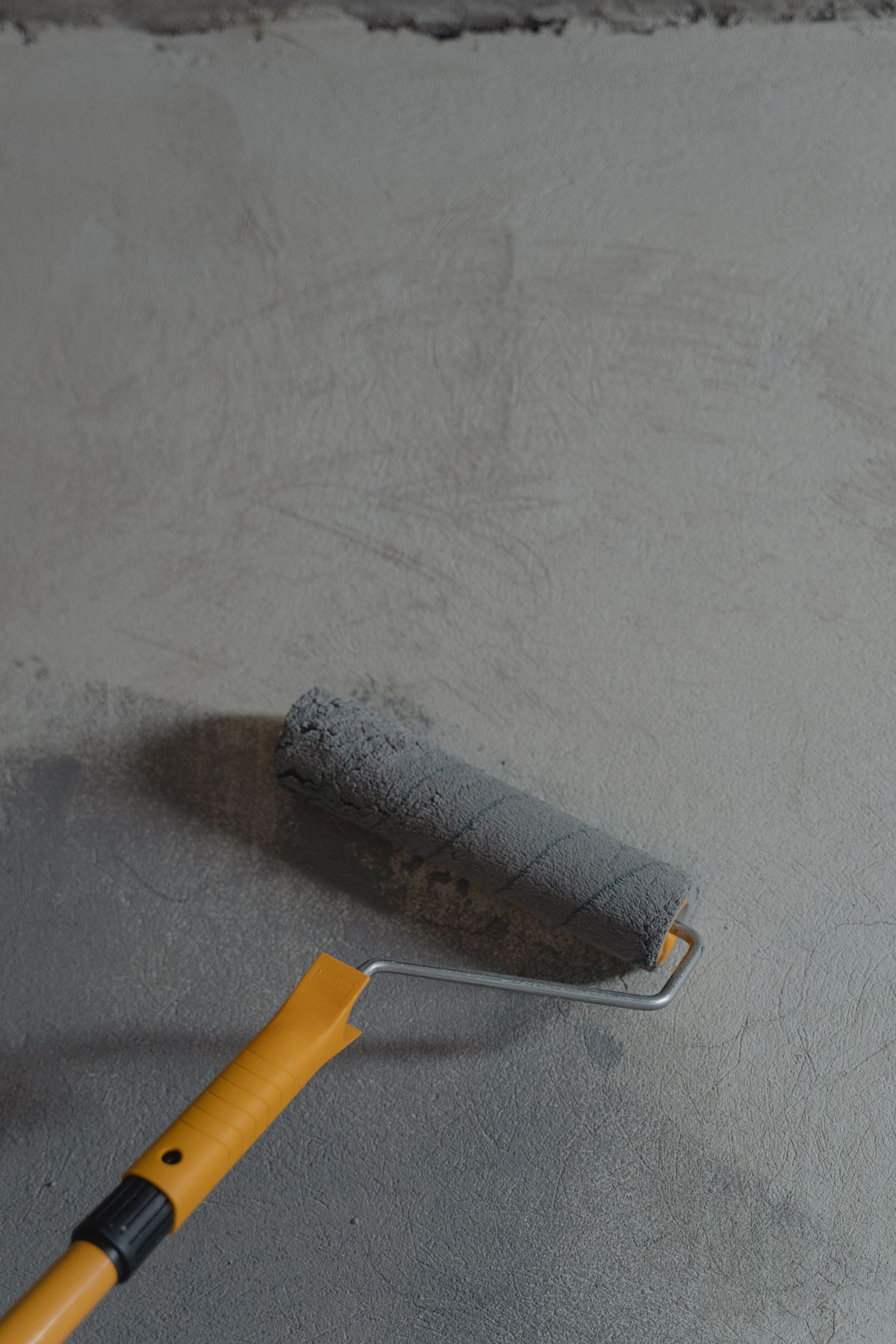 A roller laying gray primer across a troweled concrete floor before the finish goes down