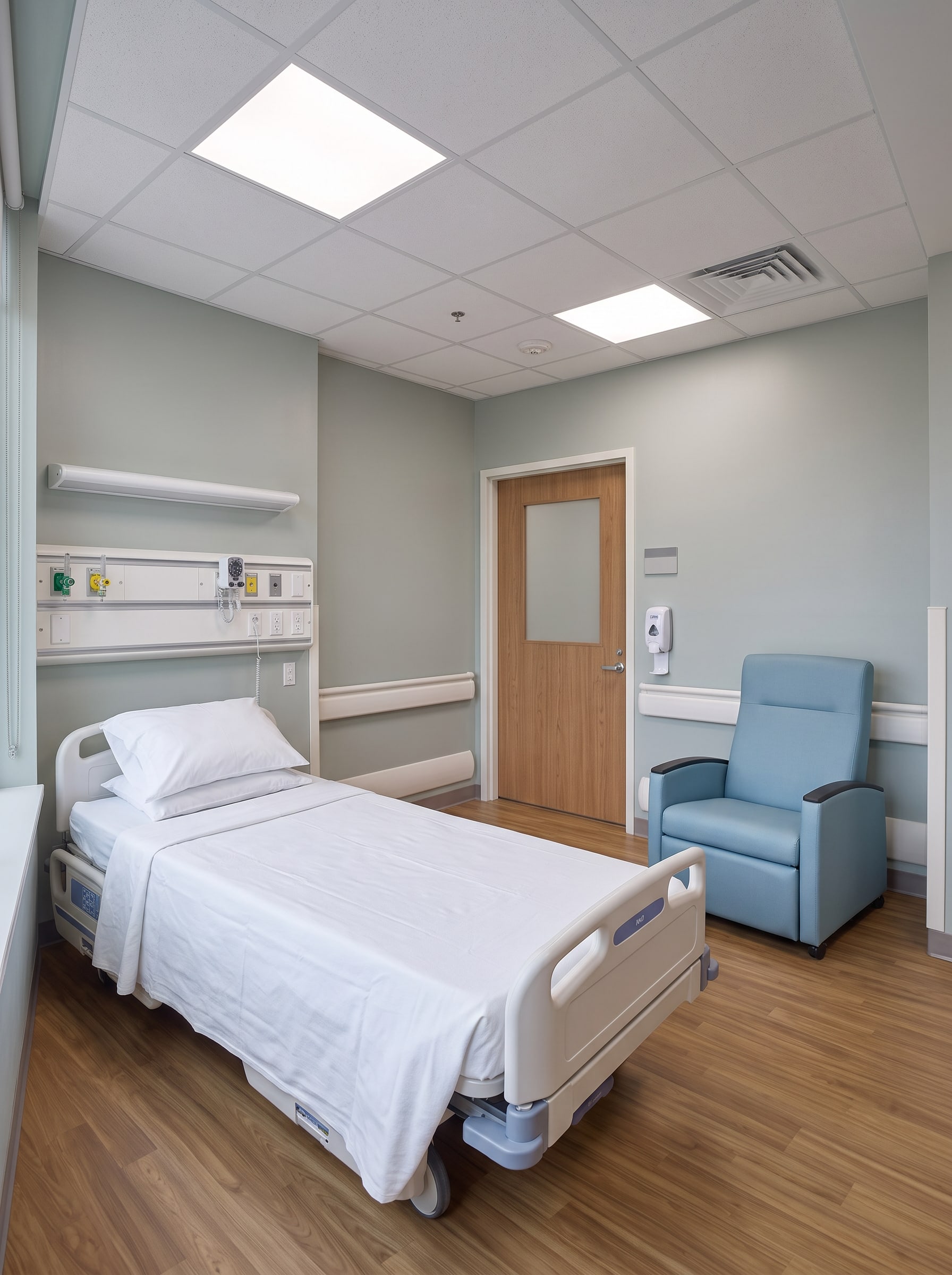 A renovated patient room seen from the window: bed, headwall, recliner and the door to the corridor