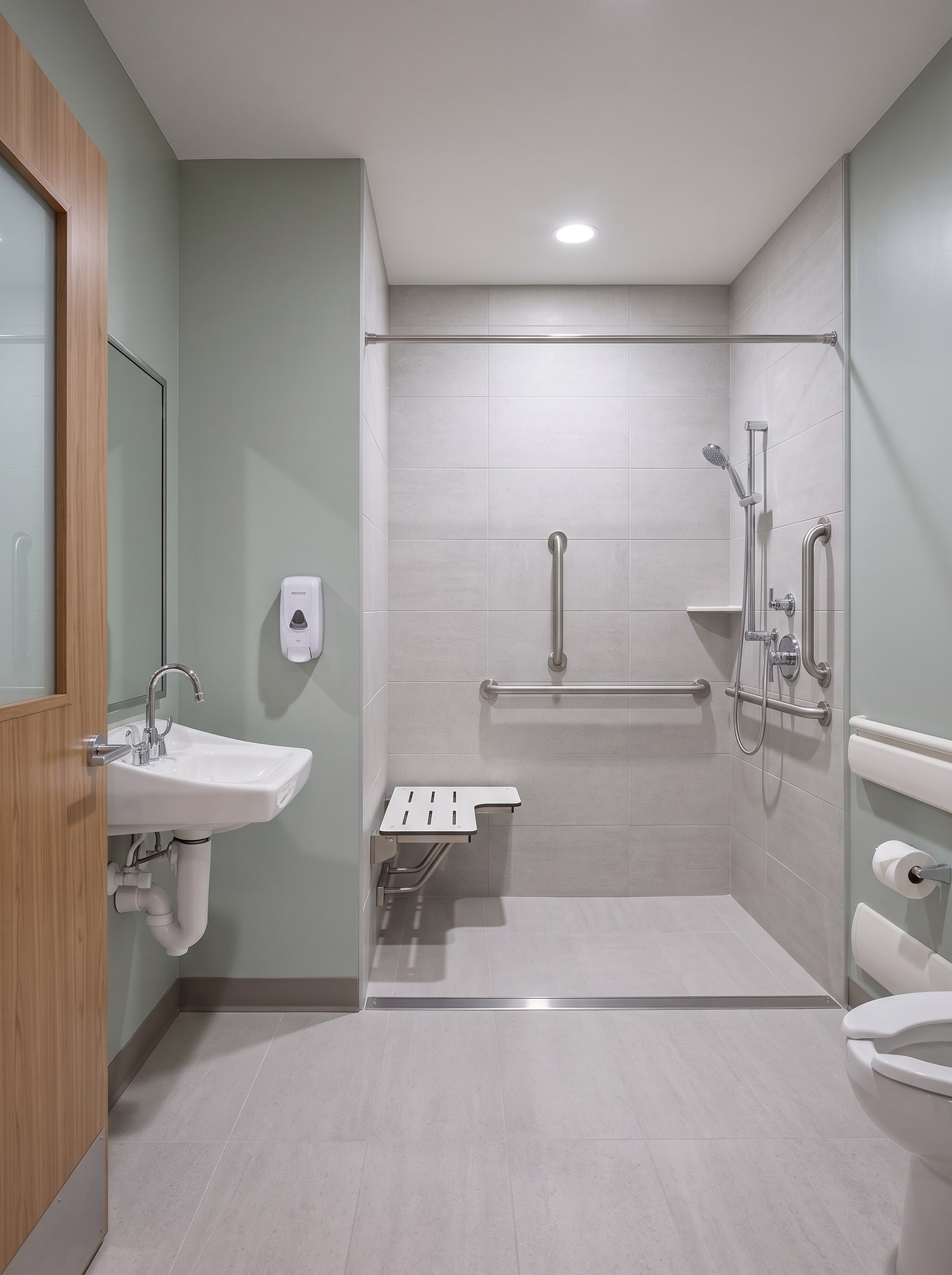 A patient bathroom: roll-in tiled shower with a fold-down seat and grab bars, wall-hung sink