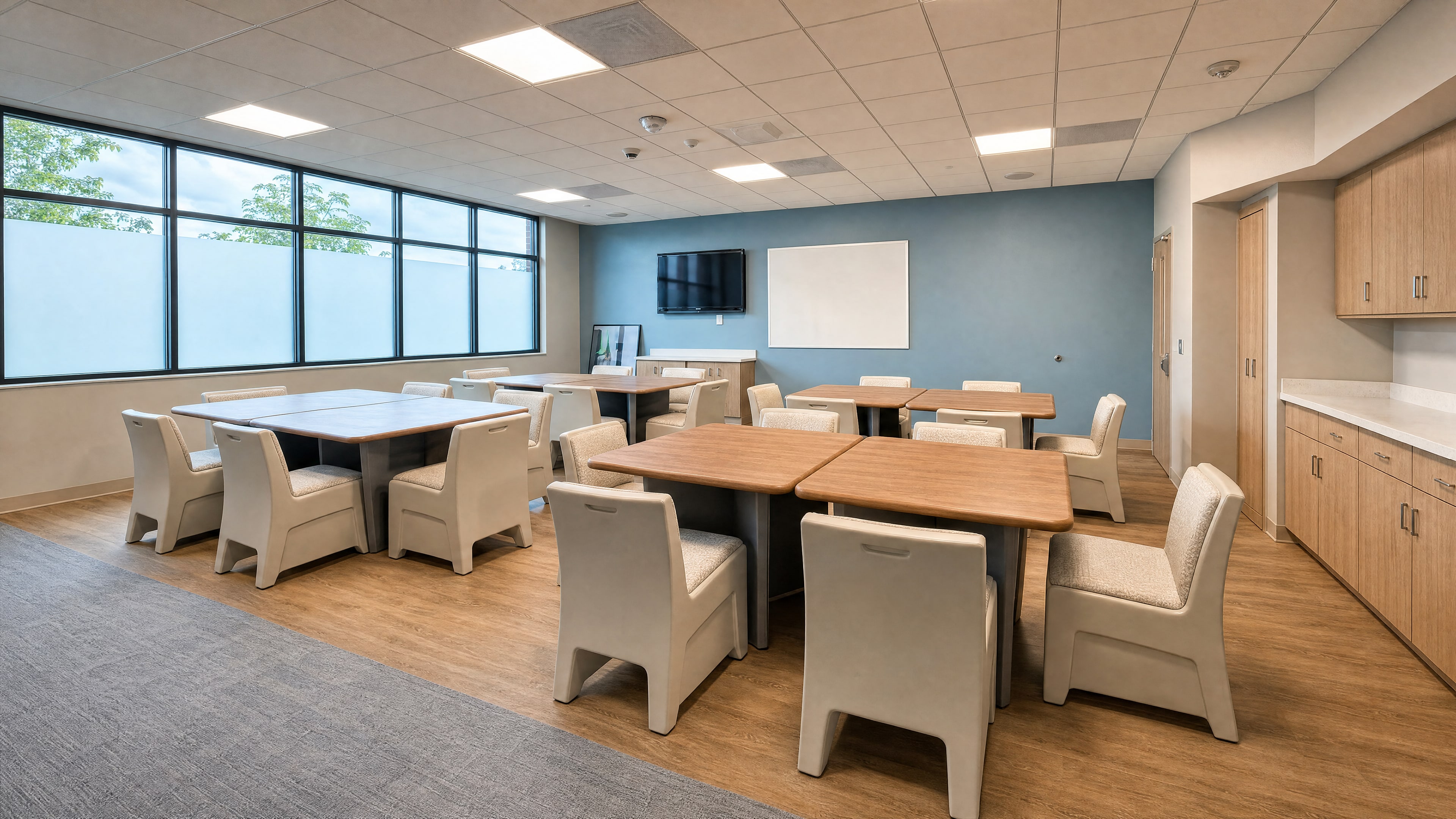 The renovated group and dining room: wood-top tables, tamper-resistant chairs, a blue accent wall and a band of windows