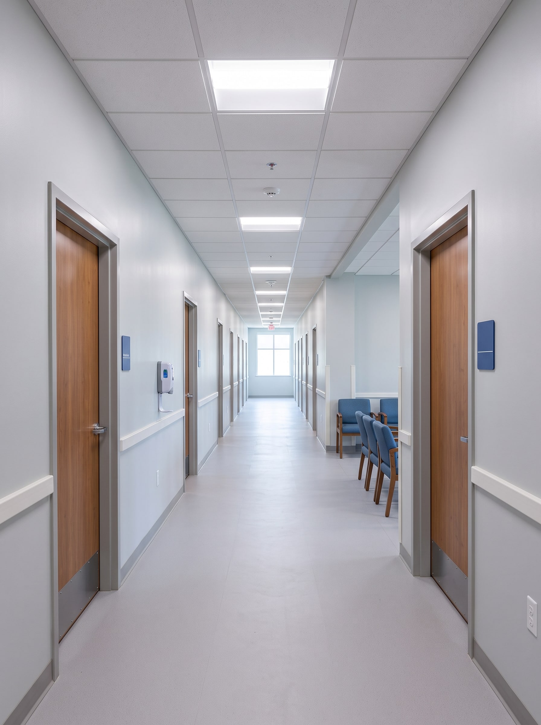 The exam room corridor: wood-veneer doors with blue room signs on both sides, a window at the far end