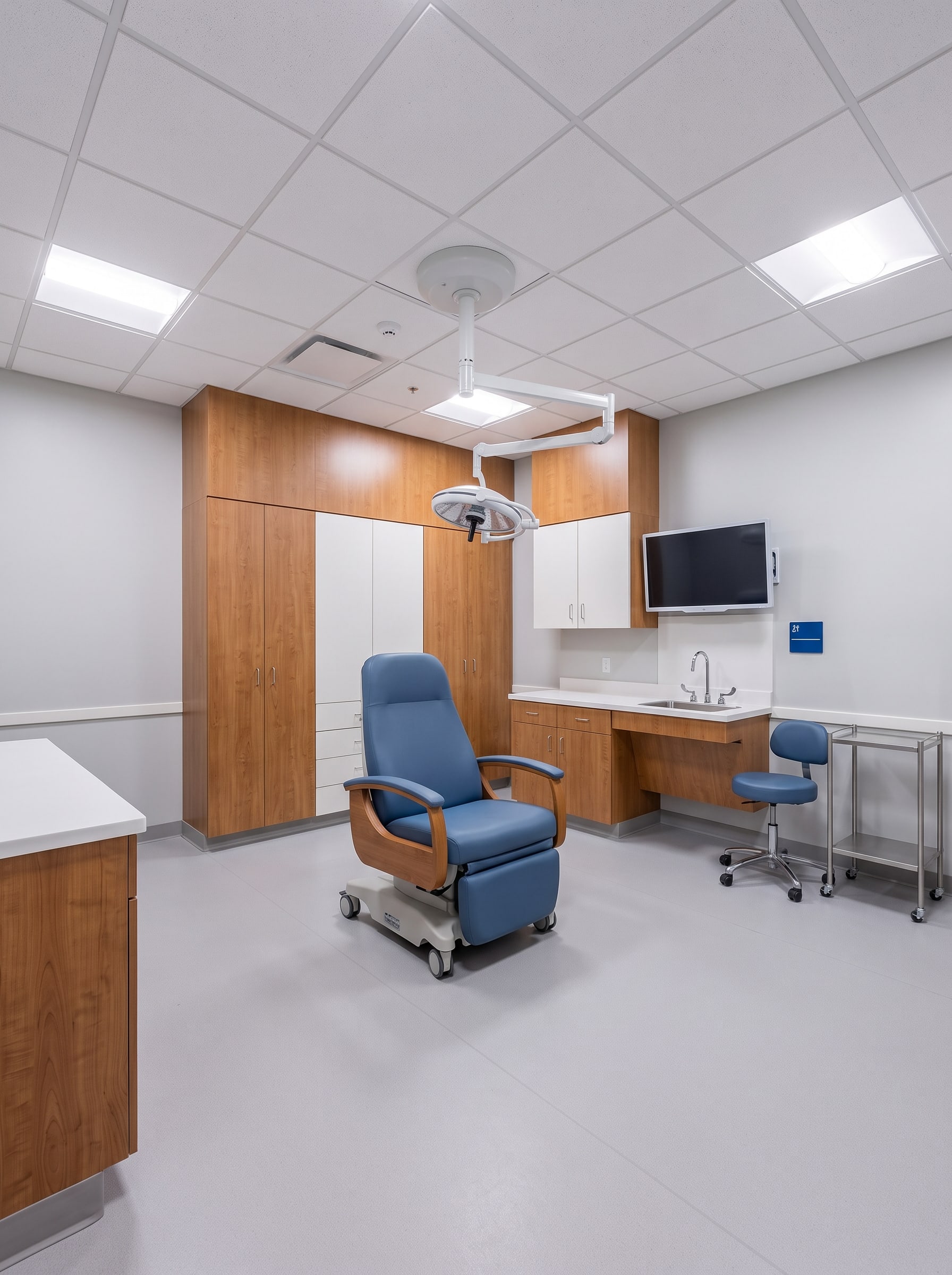 A finished treatment room at turnover: procedure chair under a ceiling-mounted exam light, full-height casework and a sink along the back wall