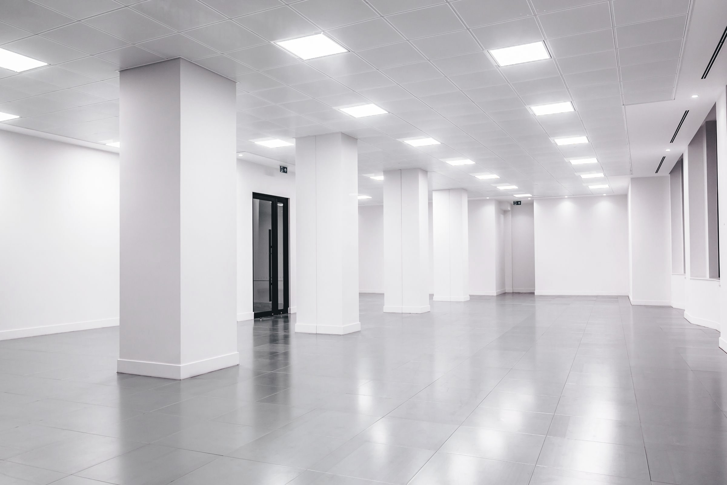 An empty, freshly finished commercial floor ready for turnover, with white walls and columns under lay-in lights