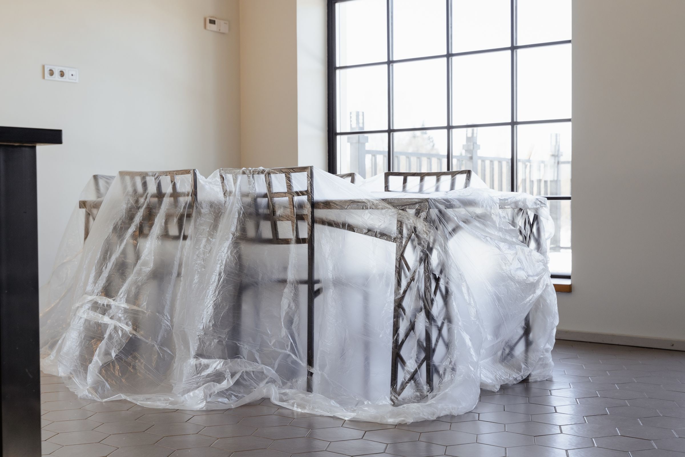 A table and chairs wrapped in clear plastic sheeting in a bright room, protected before painting begins