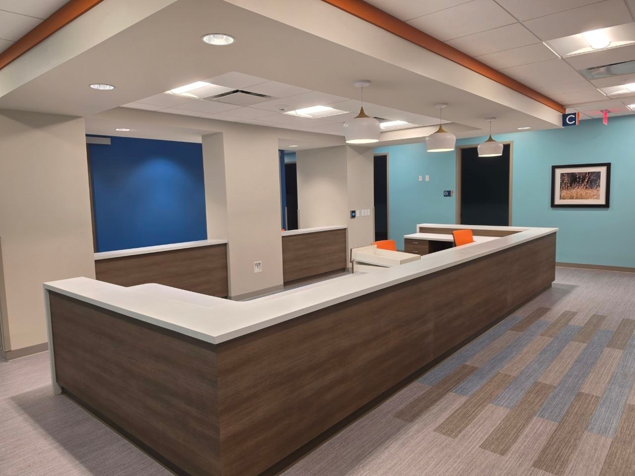 A finished nurse station with L-shaped wood casework under a soffit, blue and aqua accent walls and framed art beyond