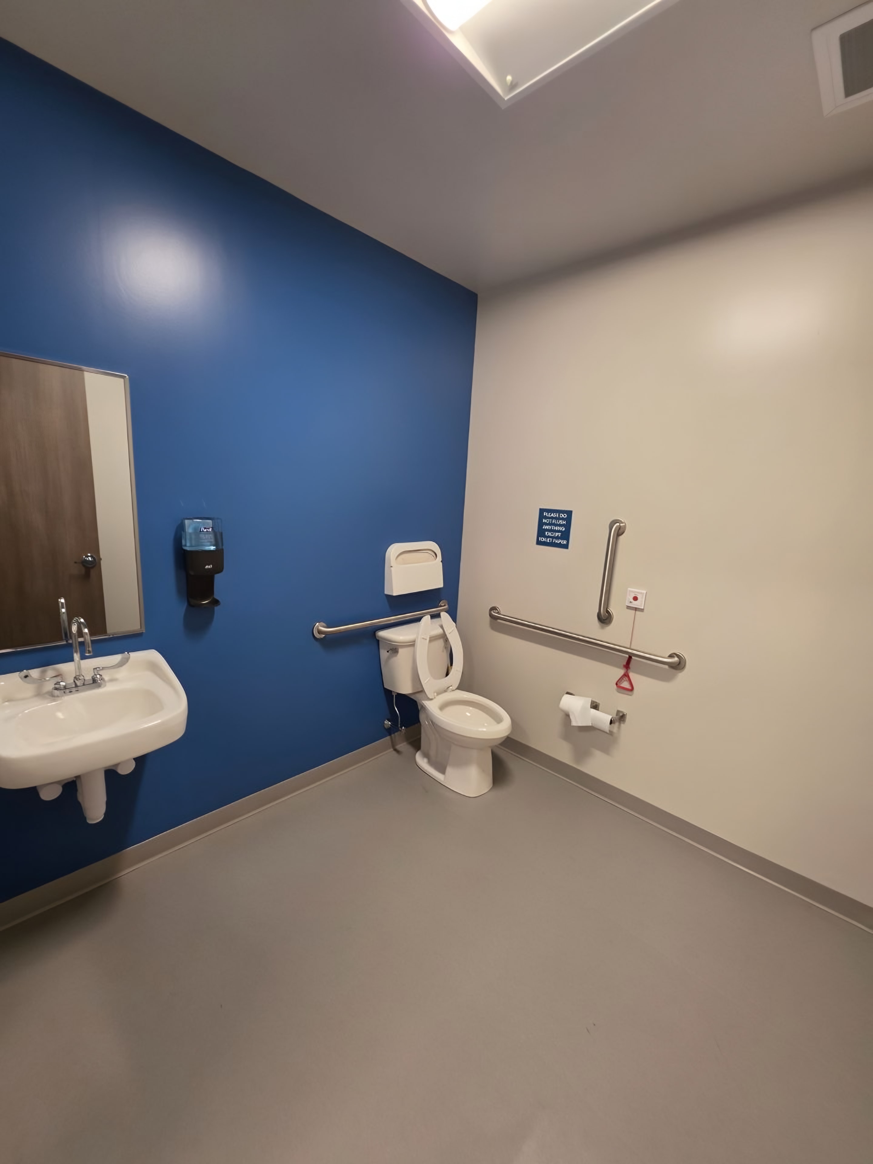 A finished accessible restroom with a blue accent wall, grab bars and coved sheet flooring