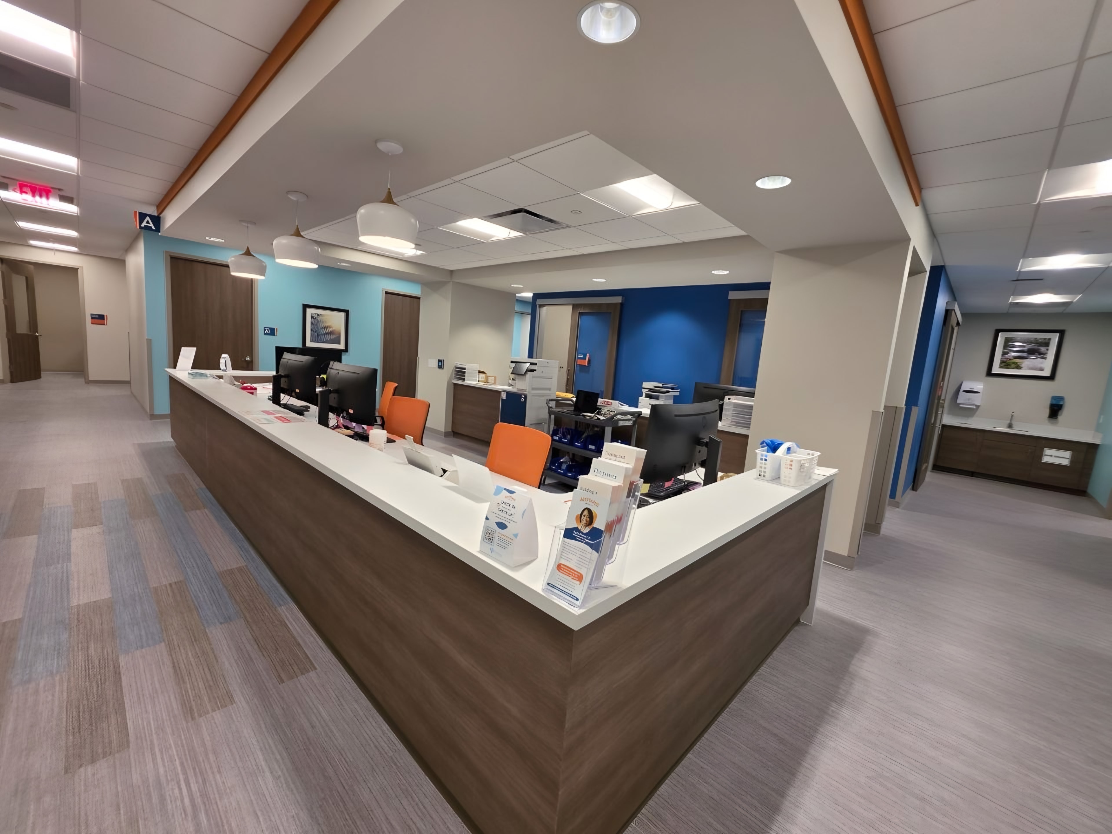 A finished outpatient clinic nurse station: L-shaped wood casework with a solid-surface top and blue and aqua accent walls