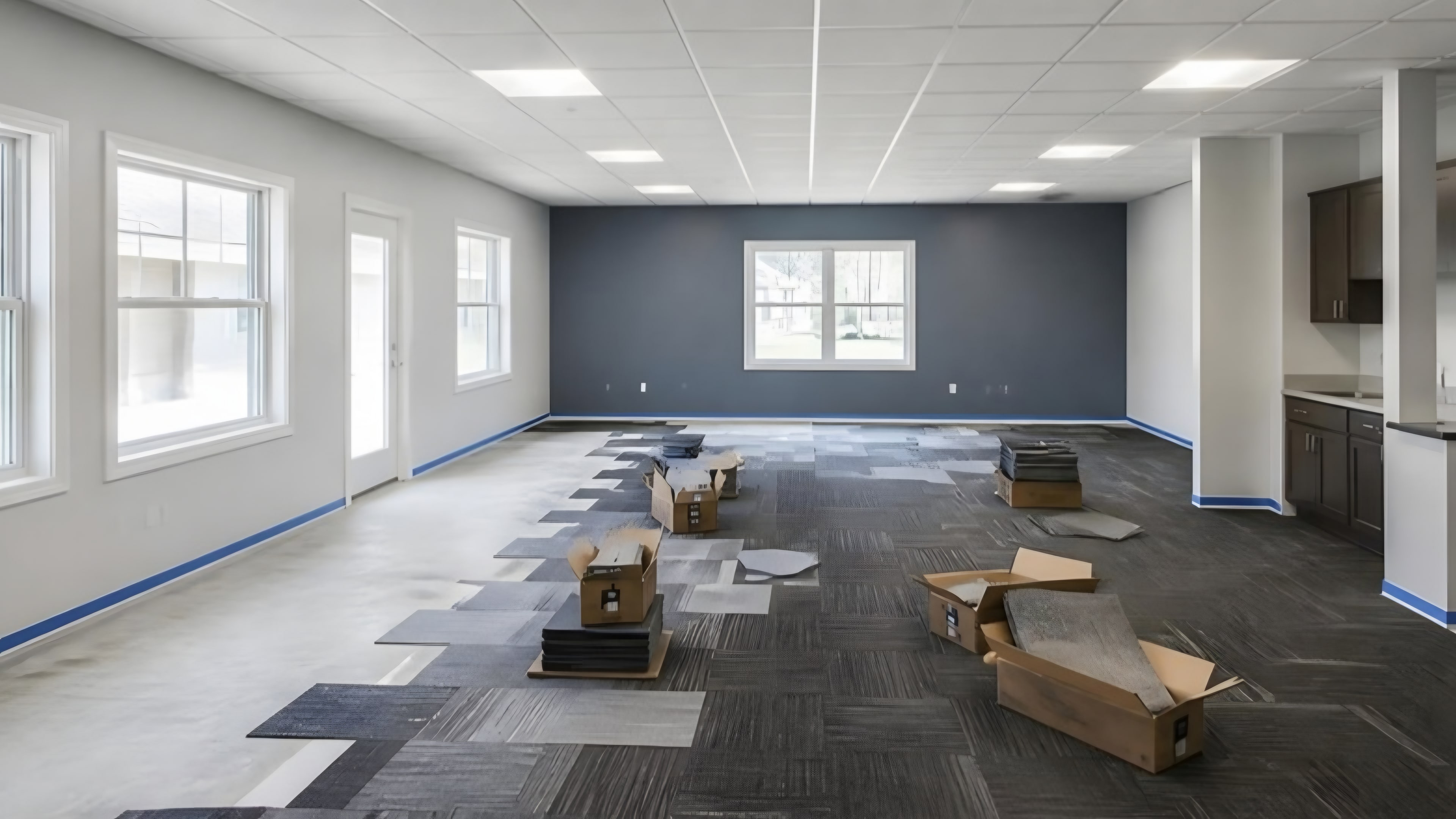 A large common room with a dark accent wall and new carpet tile being laid