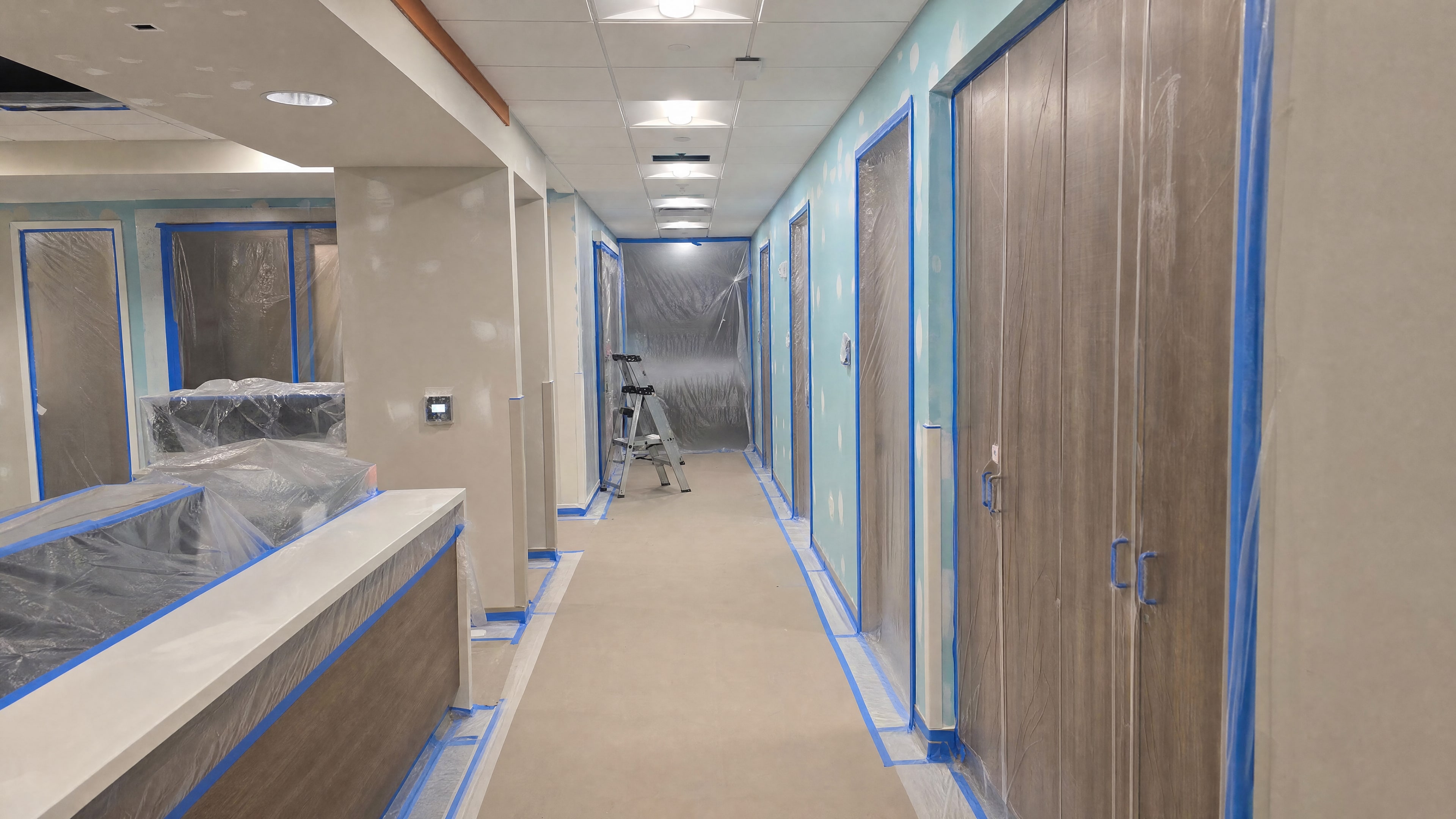 A corridor with floors papered, doors masked in plastic and patched walls