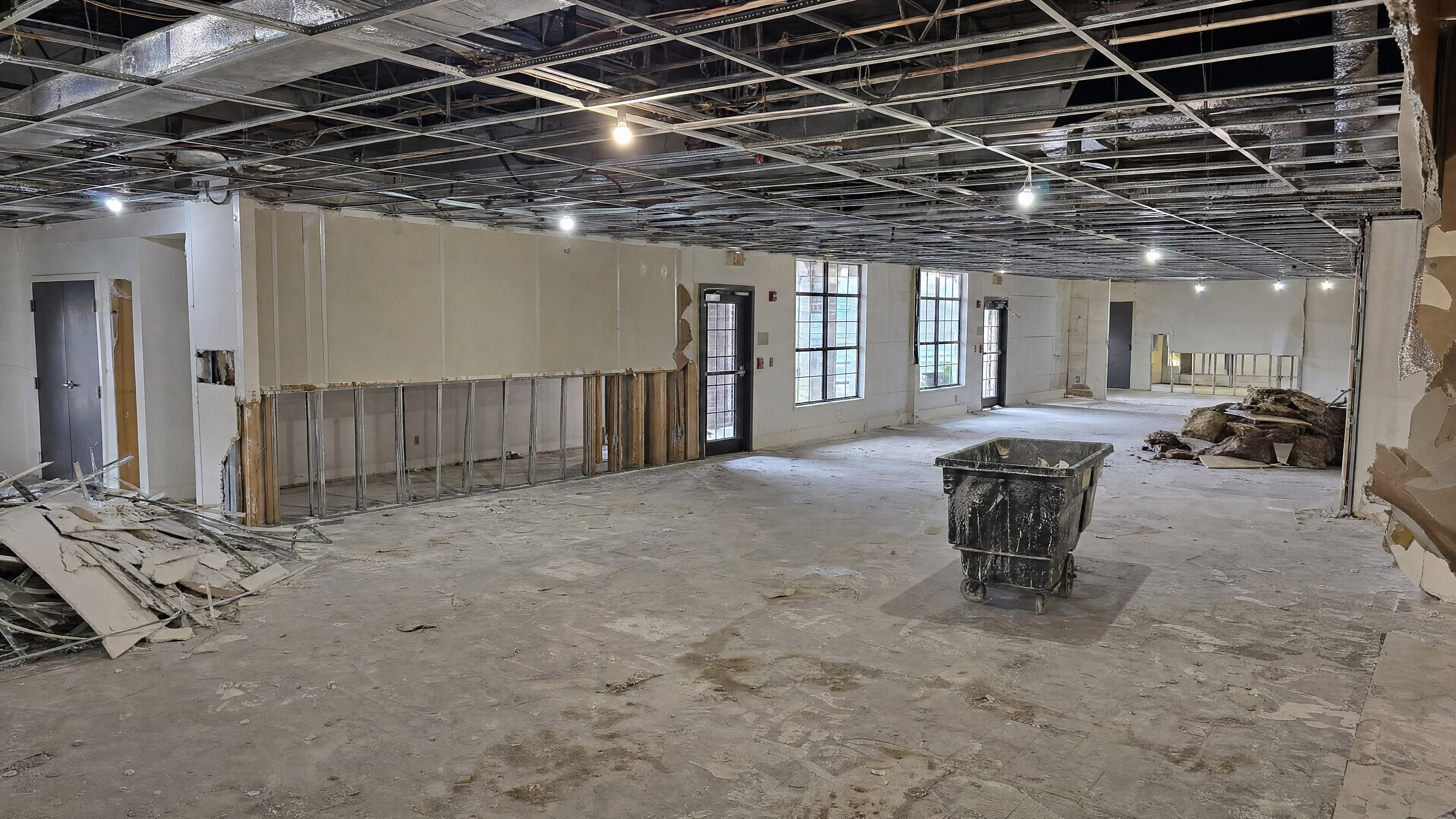 The lounge stripped for renovation: flooring removed to the slab, ceiling grid exposed and debris on a cart