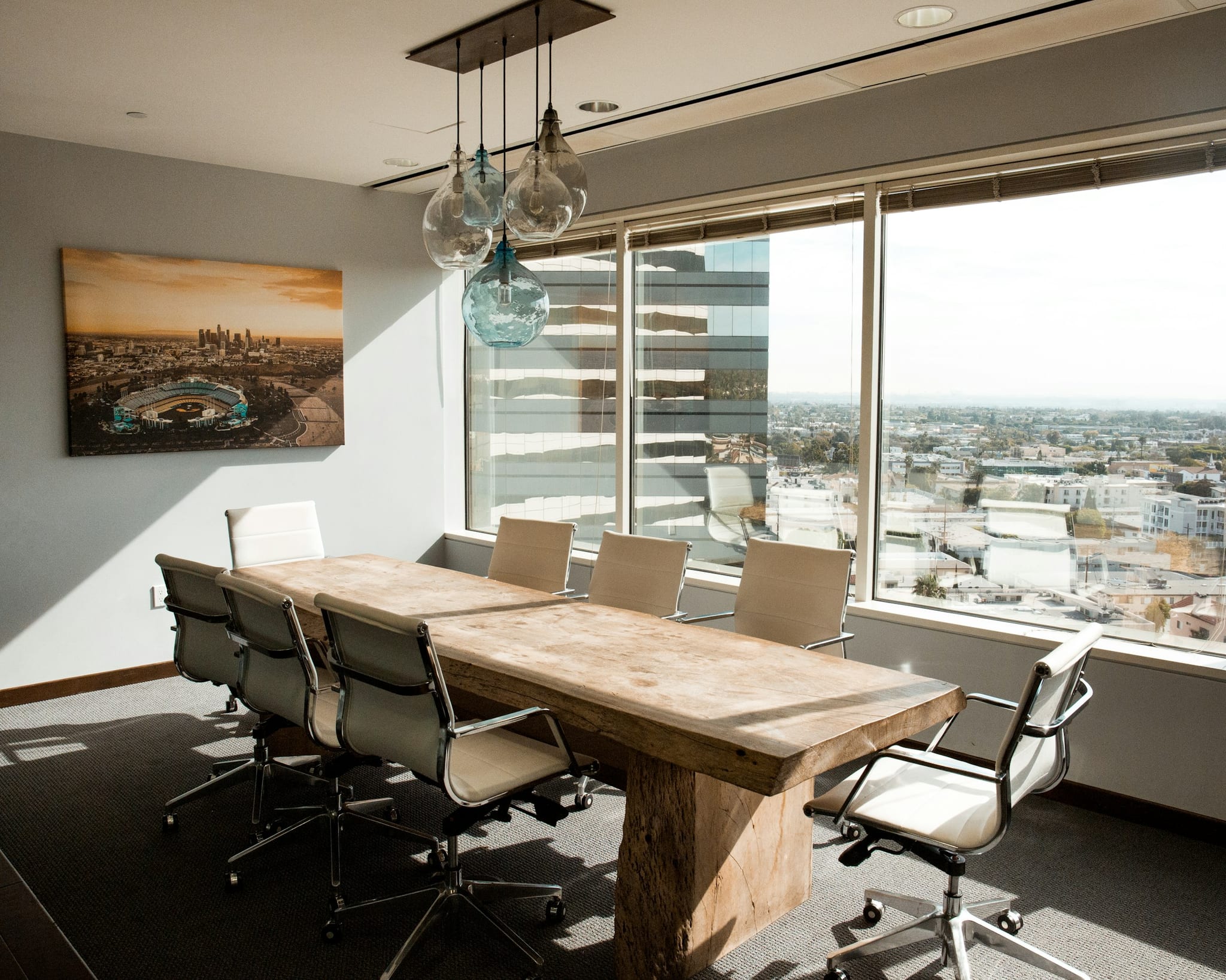 A meeting room in a finished commercial interior: a long table under pendant lights, glazed partitions onto the floor beyond, and daylight down one wall