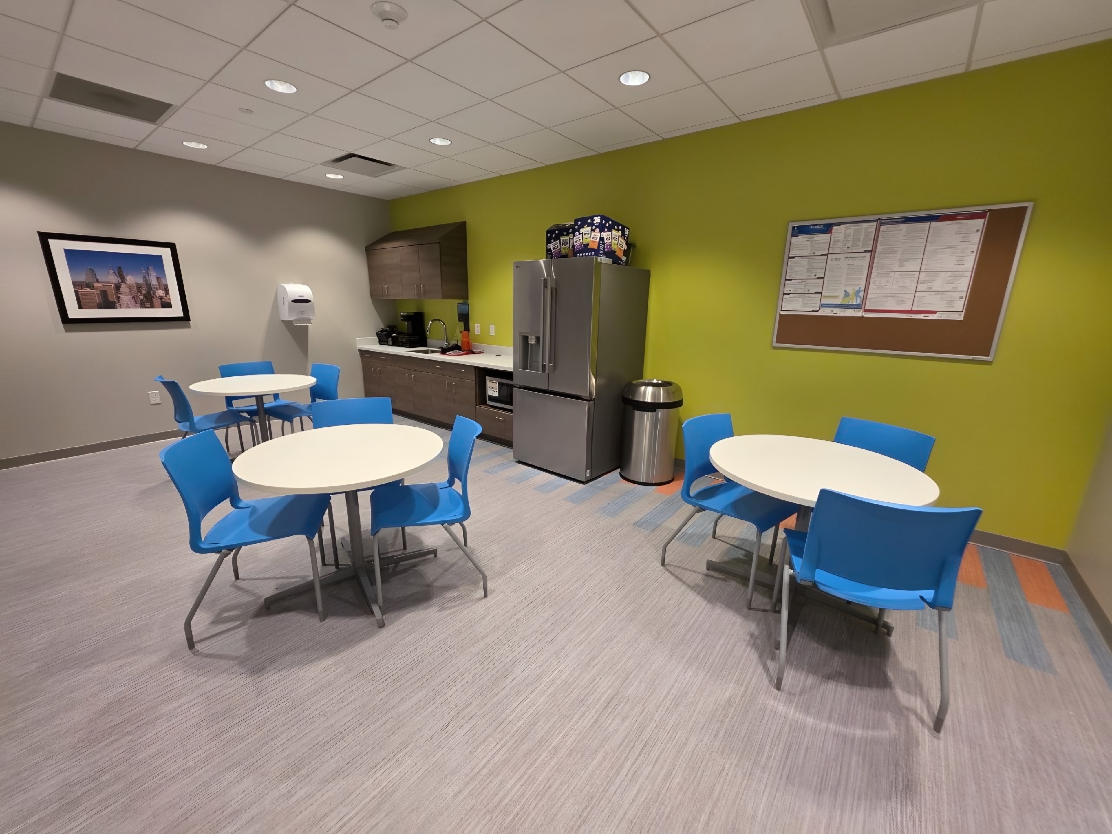 A finished staff break room with a lime accent wall and round tables