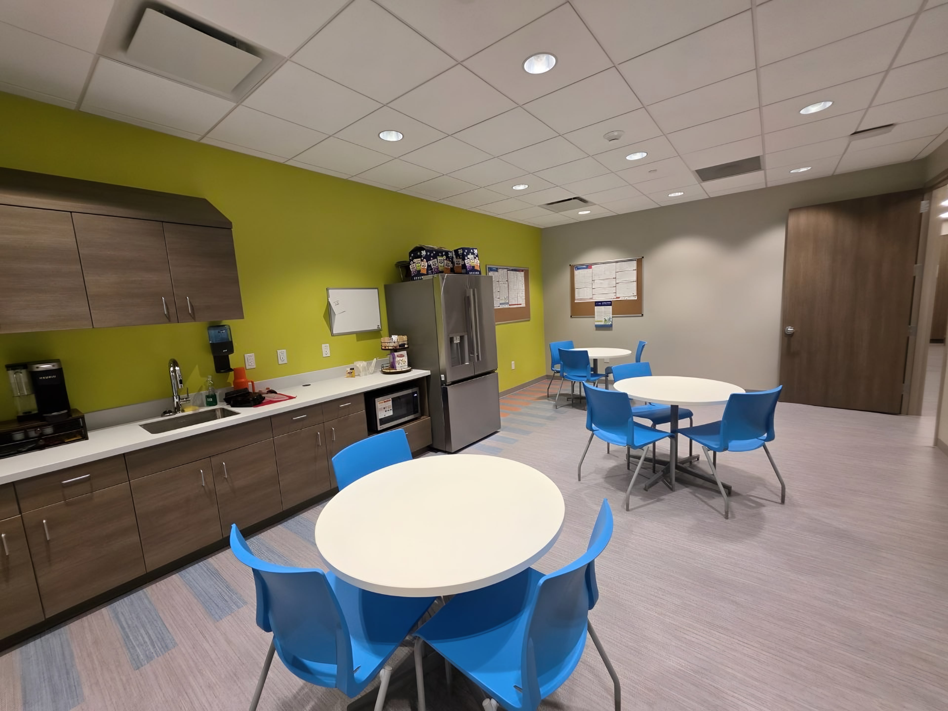 A breakroom with a green accent wall and round tables