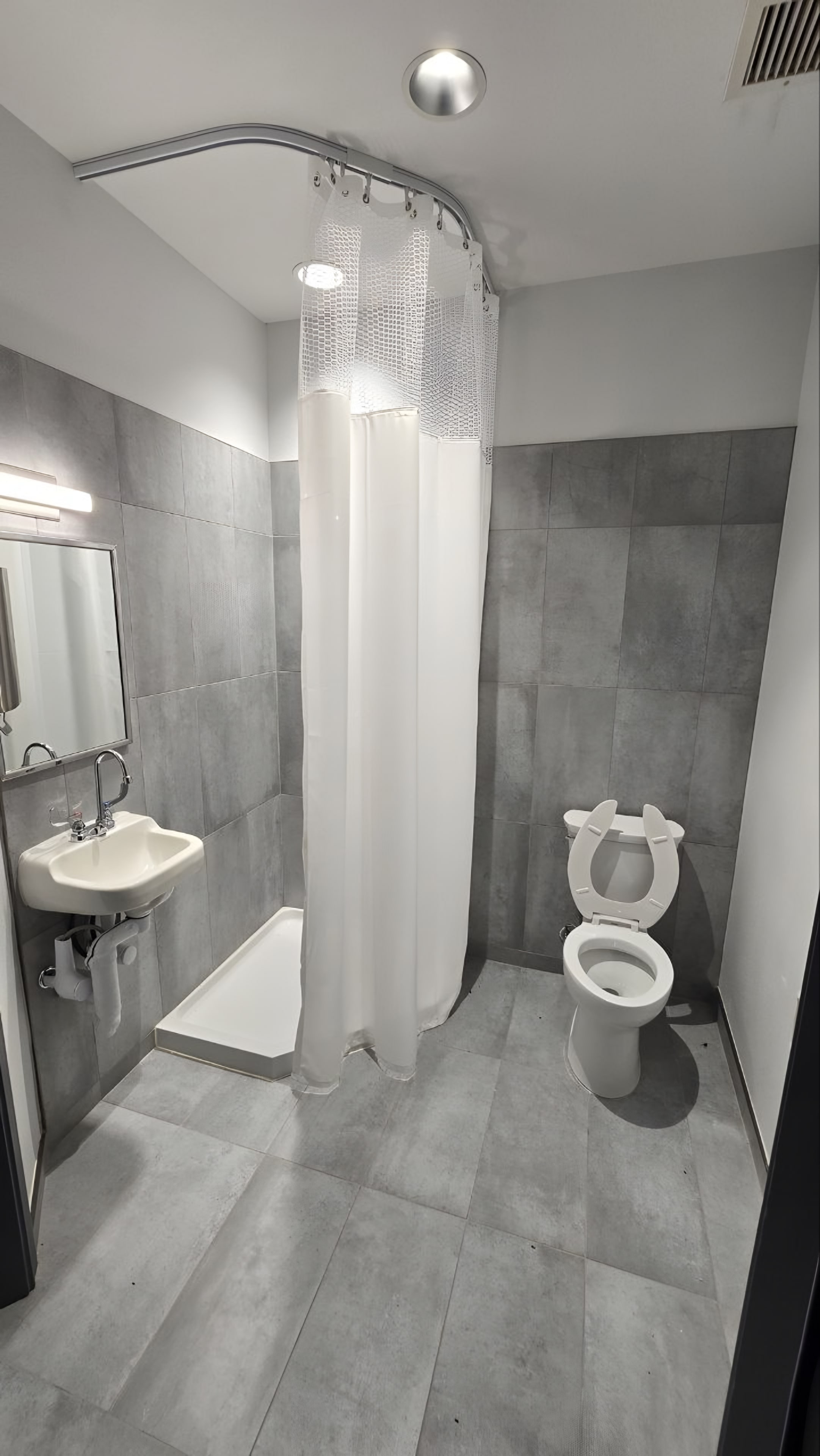 A restroom with grey tile, a wall-hung lavatory and a curtained shower