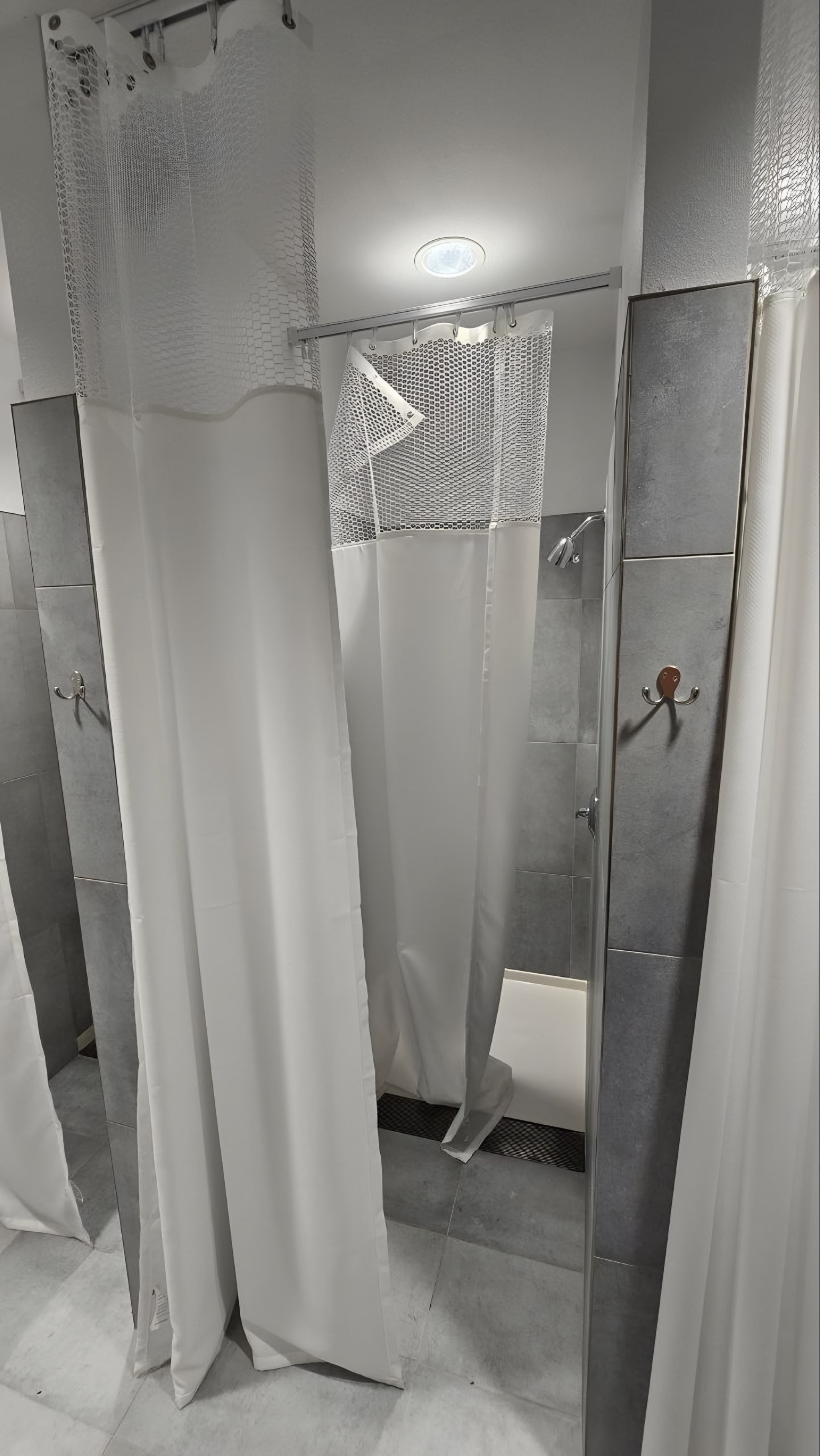 A curtained shower bay in large-format grey tile