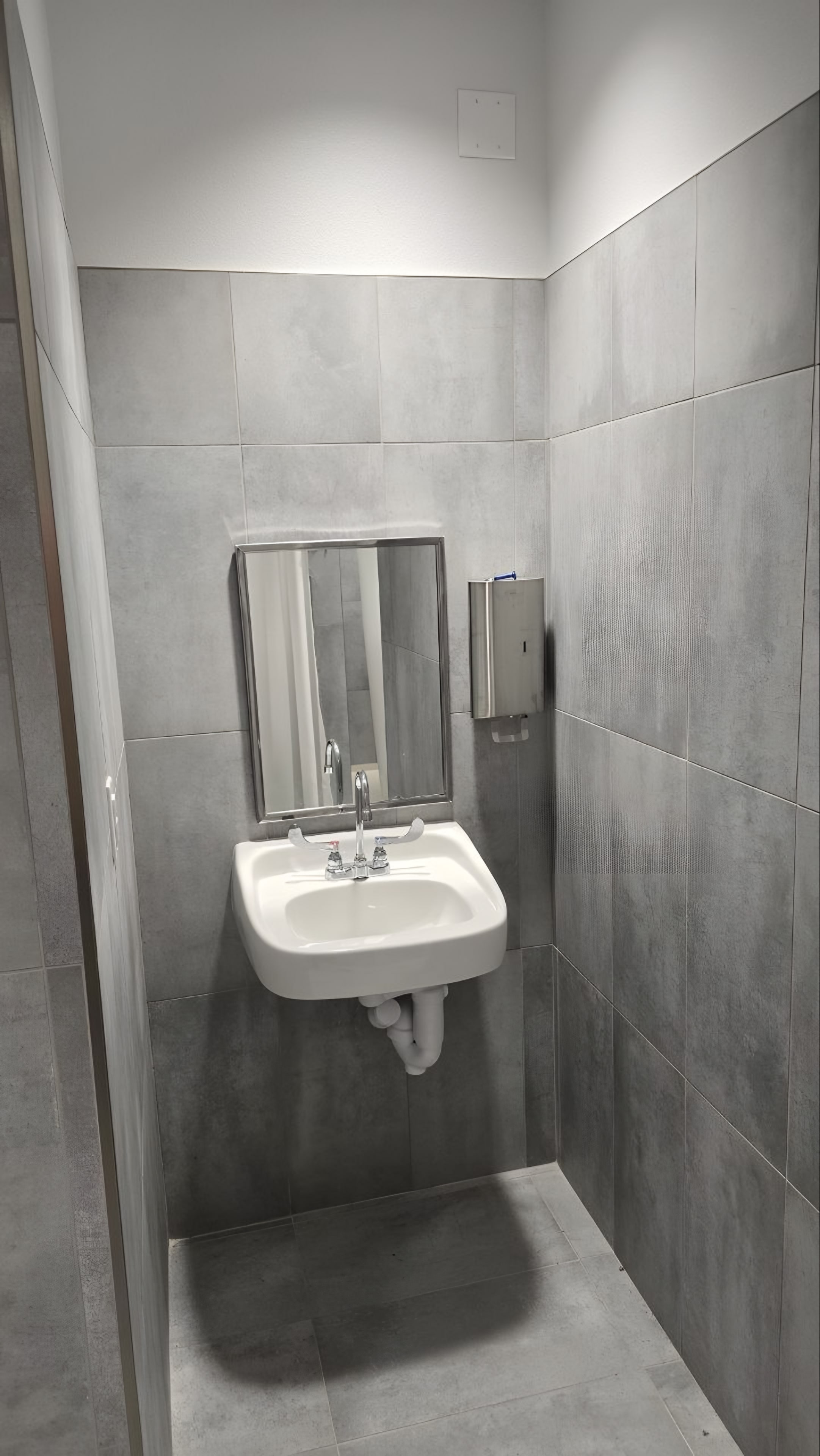 A wall-hung lavatory and mirror against grey tile