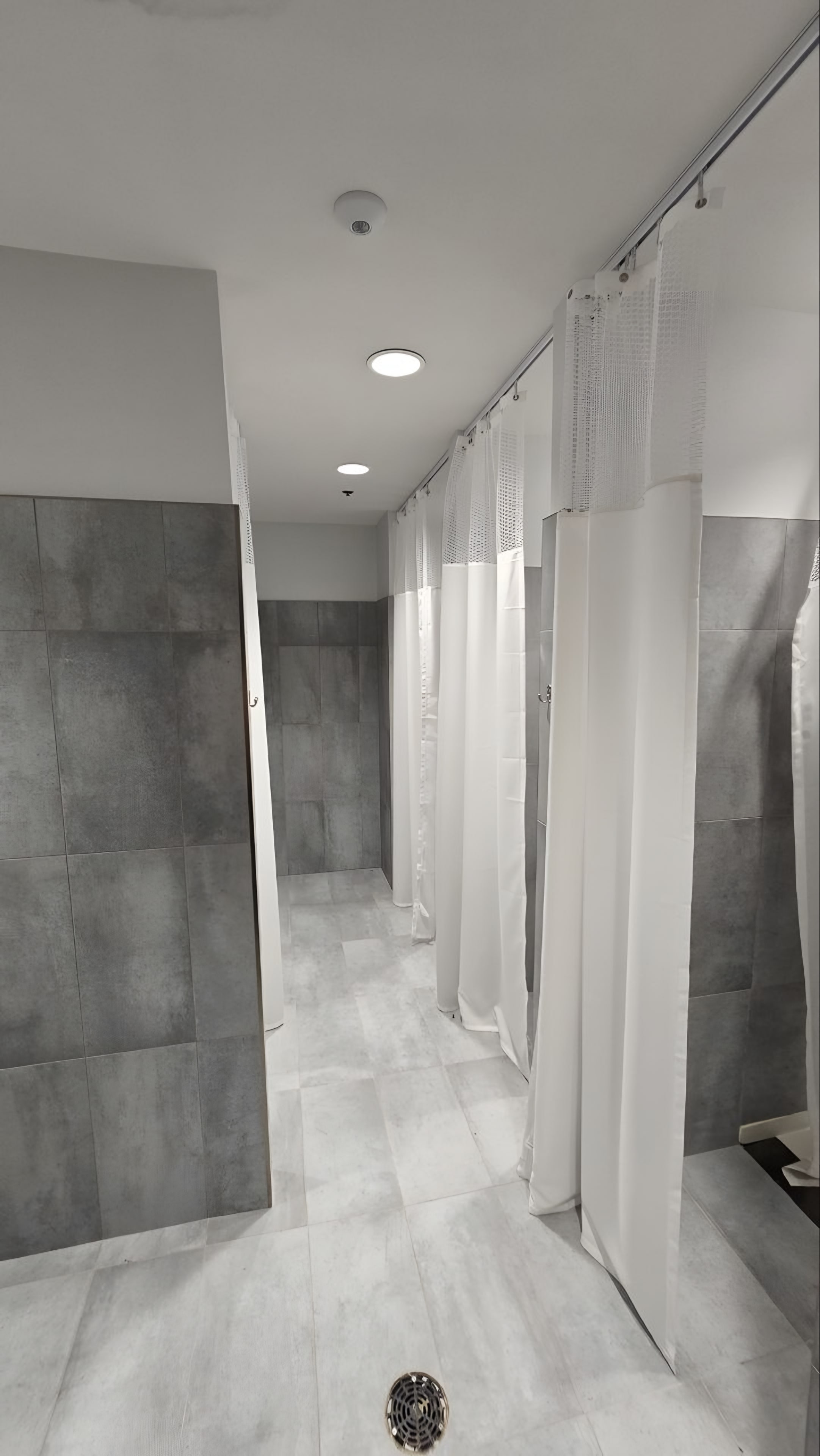 A shower room in large-format grey tile with a curtained shower bay