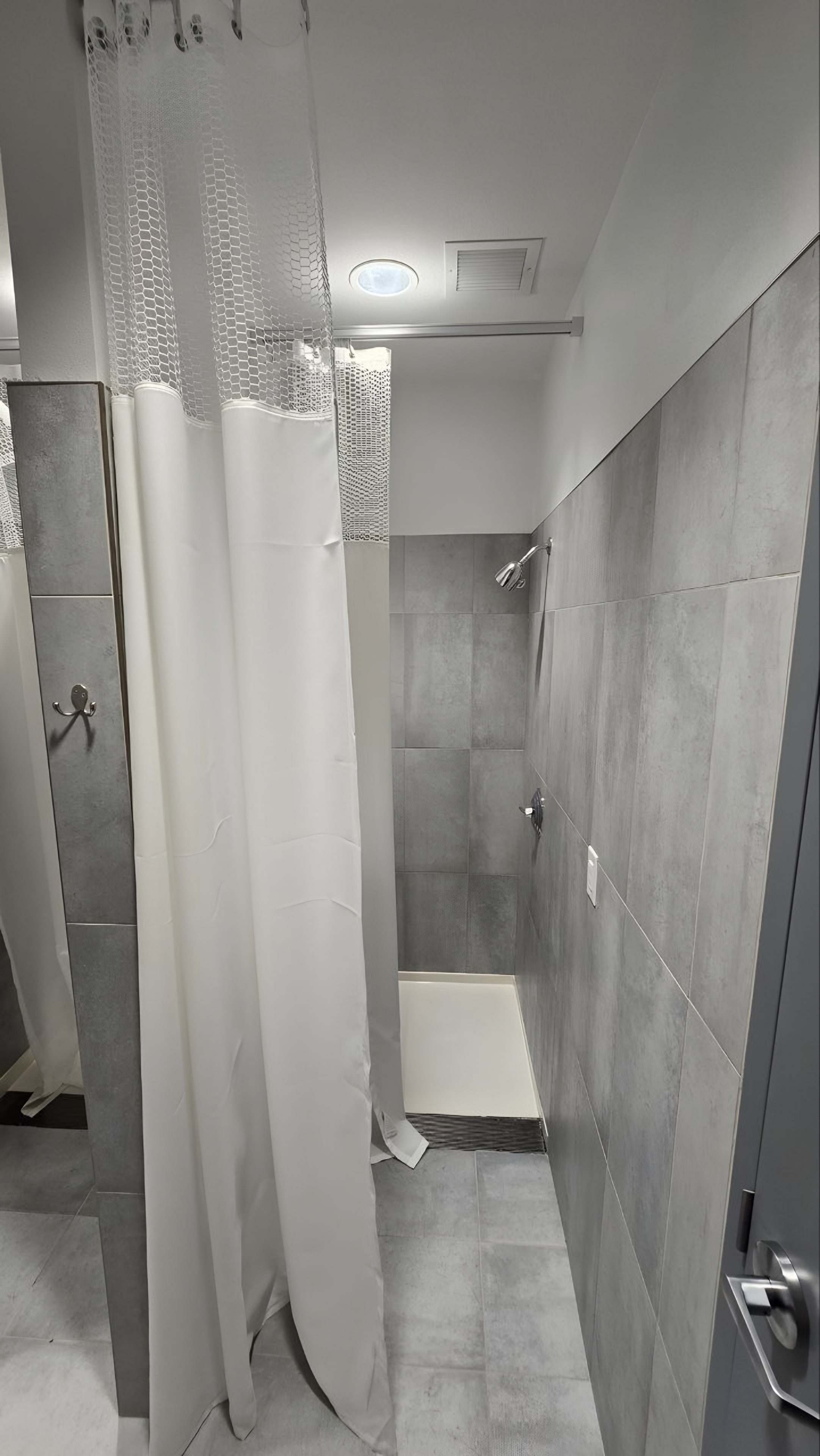 A shower with grey wall tile and a curtain