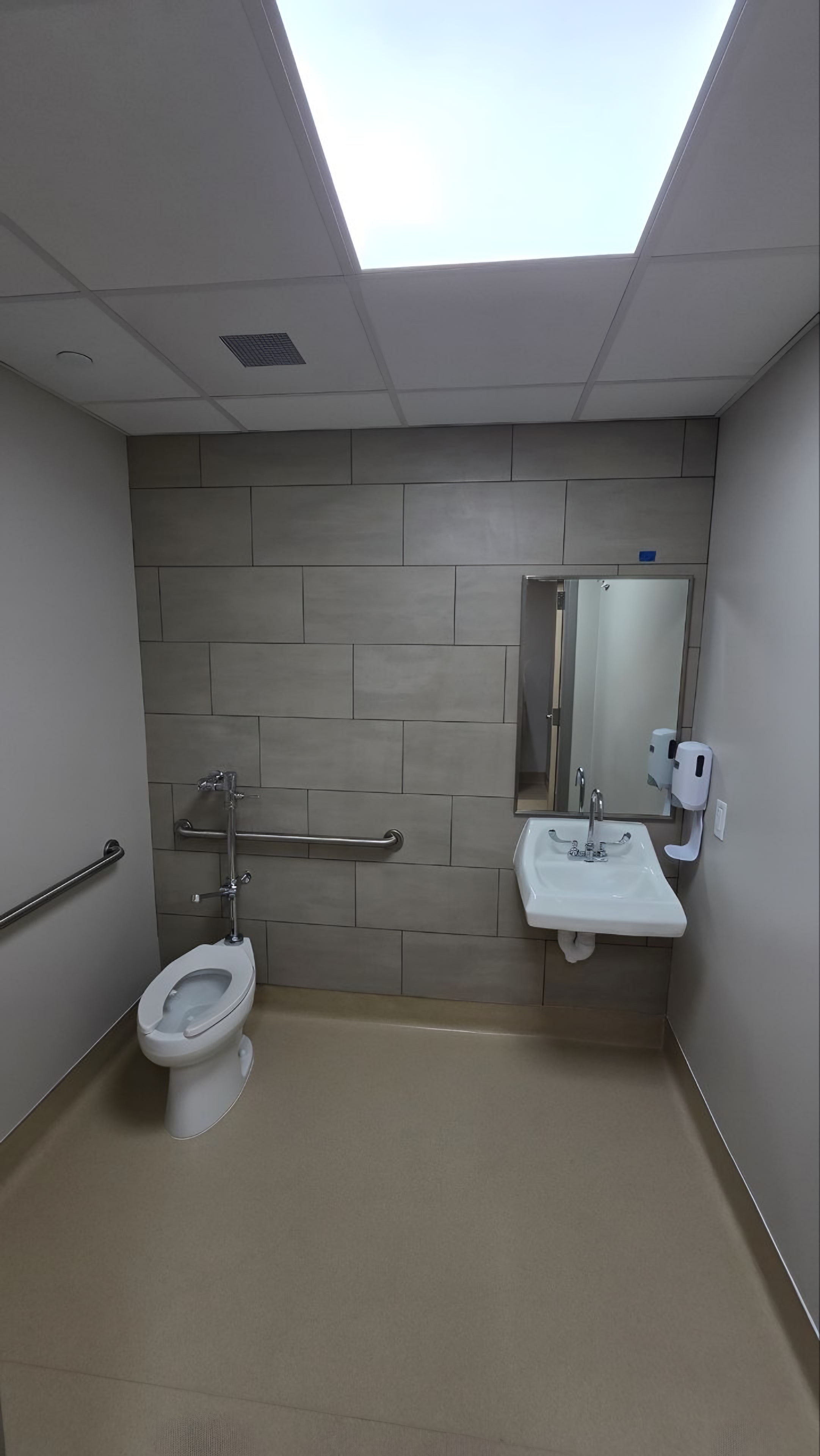 A restroom in grey tile with grab bars and a mirror