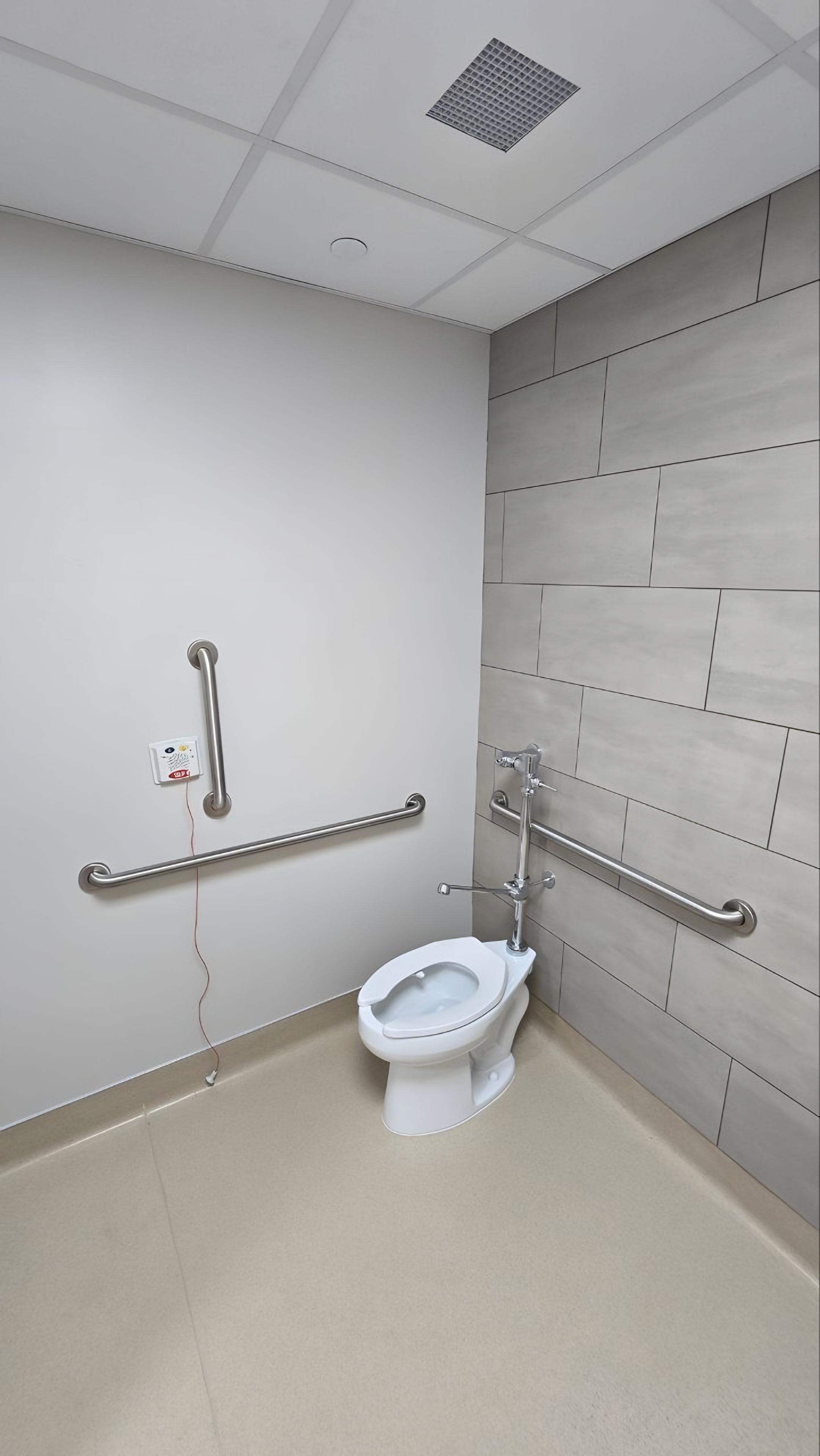 A restroom with grab bars and grey tile on one wall