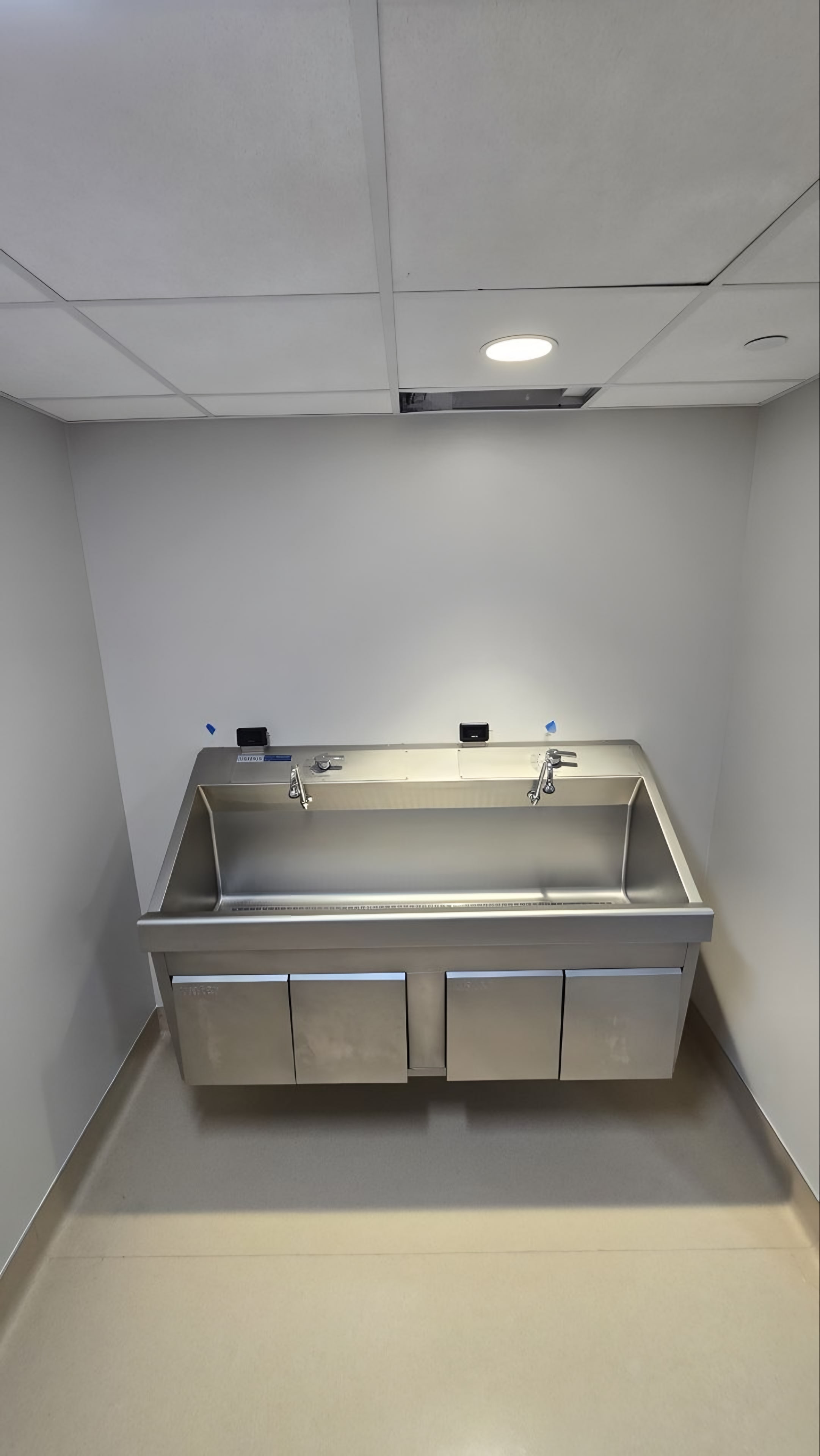 A stainless steel wash trough in a tiled room